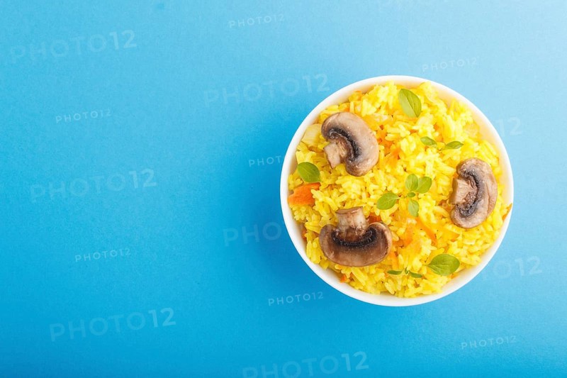 Yellow fried rice with champignons mushrooms, turmeric and oregano in white ceramic bowl on a blue pastel background. Top view, flat lay, copy space