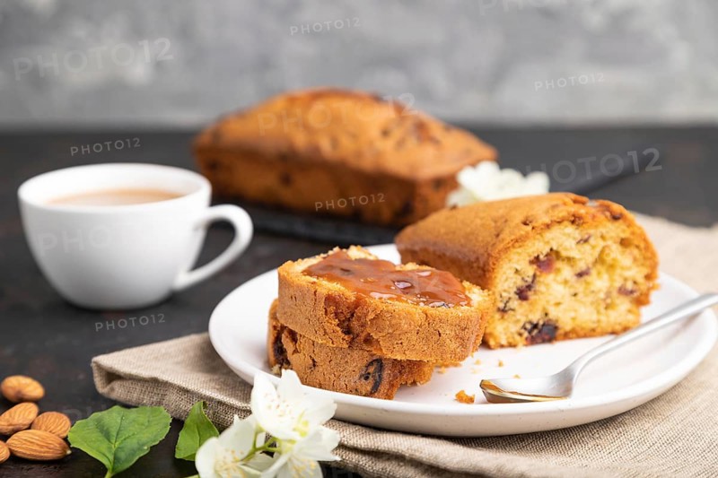 Homemade cake with raisins, almonds, soft caramel and a cup of coffee on a black concrete background and linen textile. Side view, close up, selective focus
