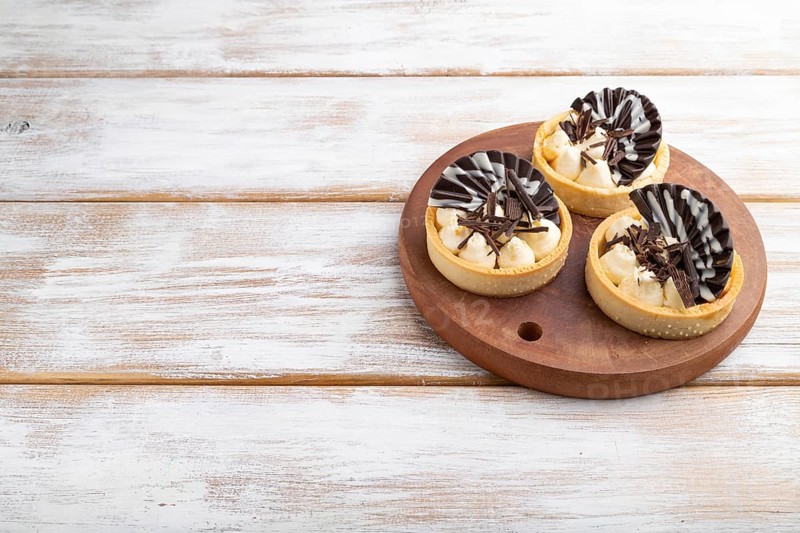 Sweet tartlets with chocolate and cheese cream on a white wooden background. side view, close up, copy space