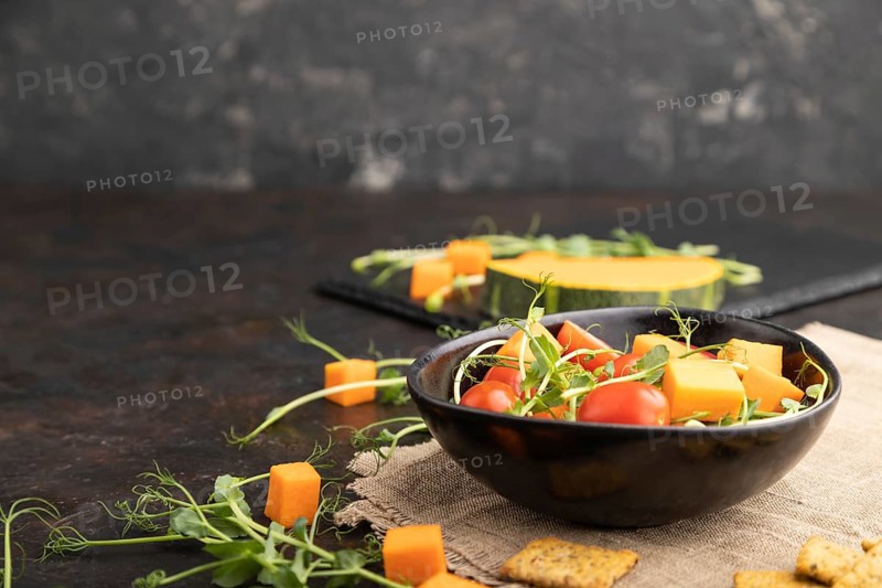 Vegetarian vegetable salad of tomatoes, pumpkin, microgreen pea sprouts on black concrete background and linen textile. Side view, copy space