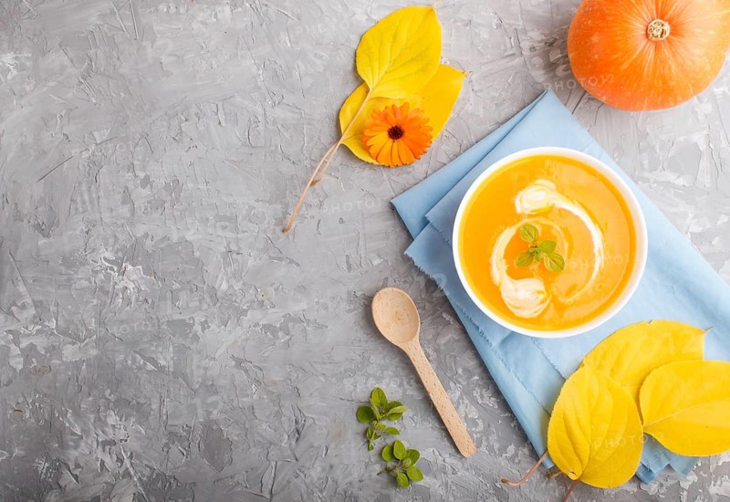 Traditional pumpkin cream soup with in white bowl on a gray concrete background with blue napkin. top view, flat lay, copy space