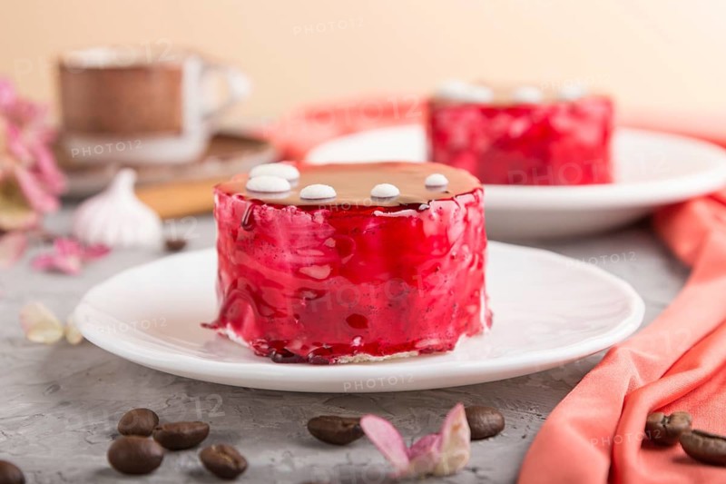 Red cake with souffle cream with cup of coffee on a gray concrete background and red textile. side view, close up. selective focus