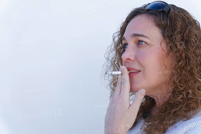 Attractive blue-eyed, curly-haired woman in profile smoking a cigarette with white background and copy space