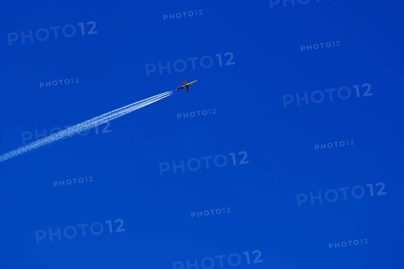 A passenger plane with vapour trail high in the blue sky