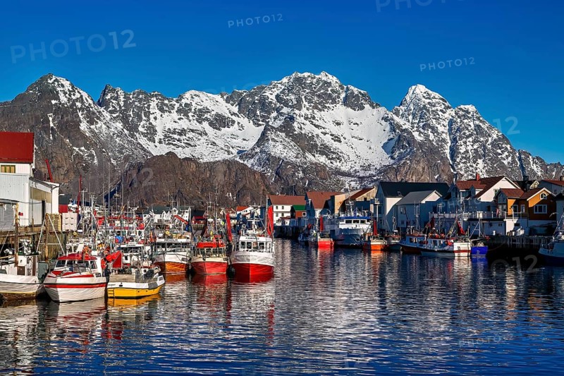 Bunte Boote und Gebaeude vor schneebedeckten Bergen in einem Hafen, Im Hafen von Henningsvaer auf den Lofoten