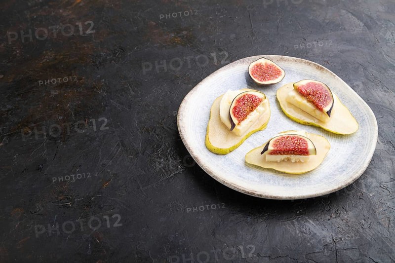 Summer appetizer with pear, cottage cheese, figs and honey on ceramic plate on a black concrete background. Side view, copy space