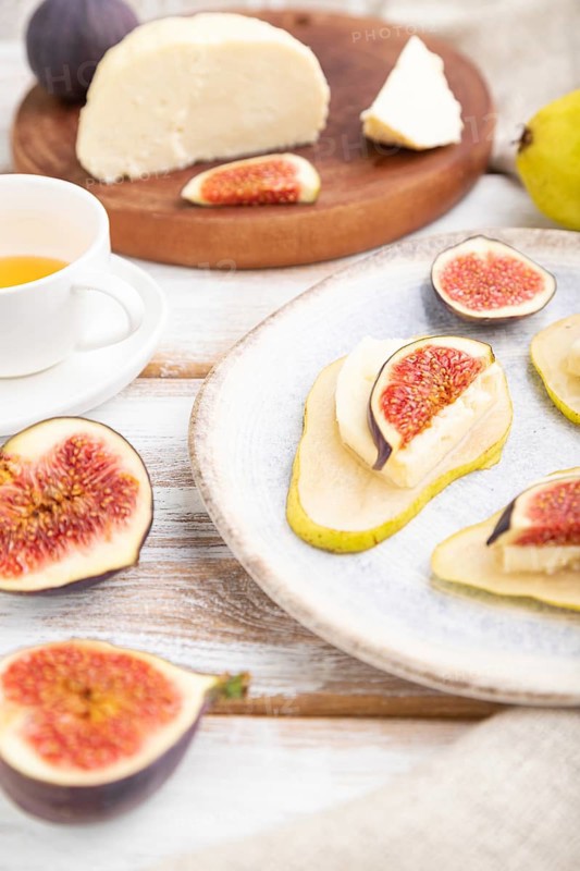 Summer appetizer with pear, cottage cheese, figs and honey on a white wooden background and linen textile. Side view, close up, selective focus