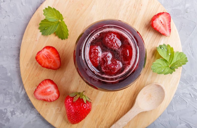 Strawberry jam in a glass jar with berries and leaves on gray concrete background. Homemade, top view, flat lay