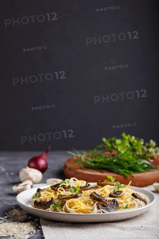 Rice noodles with champignons mushrooms, egg sauce and oregano on white ceramic plate on a black concrete background. side view, selective focus, copy space