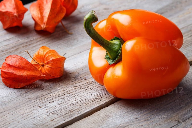 Orange pepper and red physalis on rustic wooden background with copy space