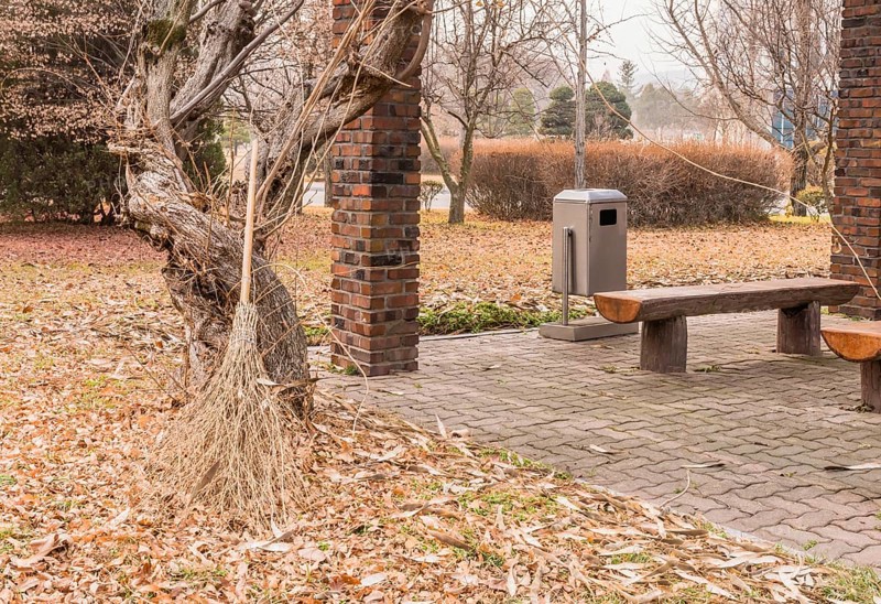 Old straw broom leaning against gnarly tree next to covered park benches in South Korea