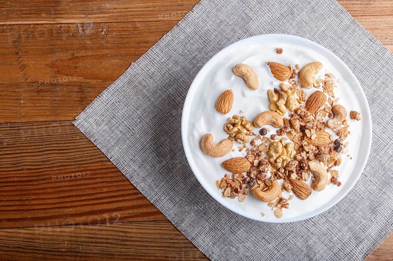 White plate with greek yogurt, granola, almond, cashew, walnuts on brown wooden background. top view. copy space