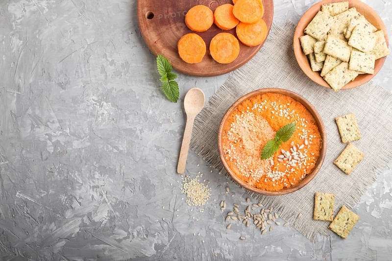 Carrot cream soup with sesame seeds and snacks in wooden bowl on a gray concrete background with linen textile. top view, flat lay, copy space