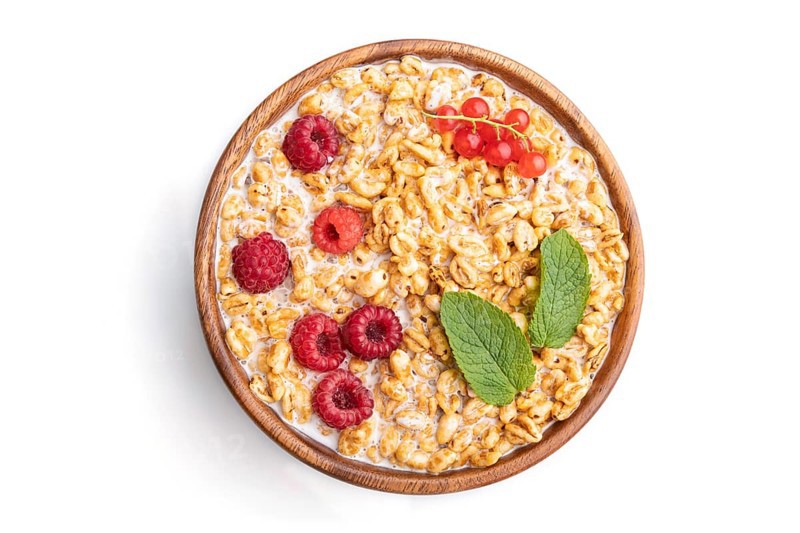 Wheat flakes porridge with milk, raspberry and currant in wooden bowl isolated on white background. Top view, flat lay, close up