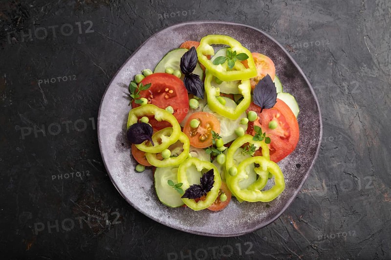 Vegetarian salad from green pea, tomatoes, pepper and basil on a black concrete background. top view, close up, flat lay
