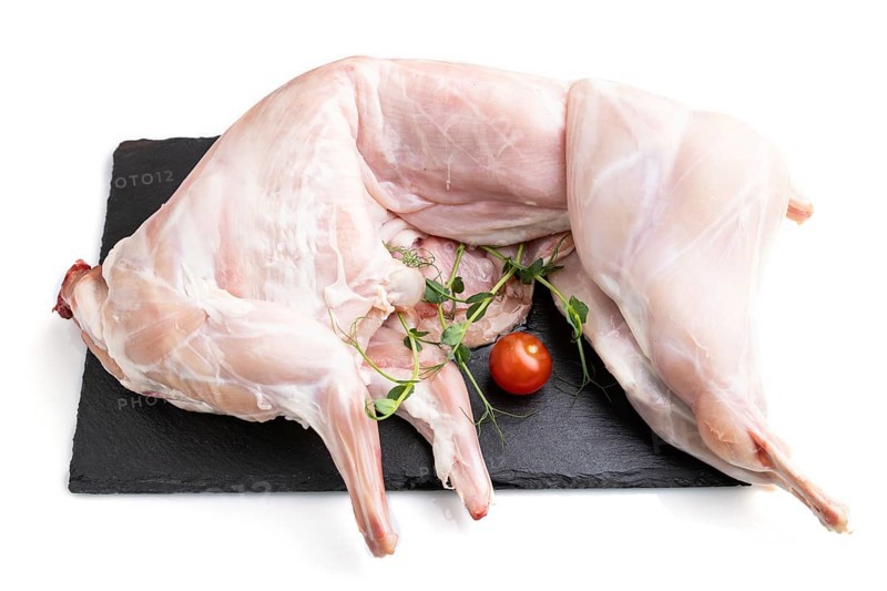 Whole raw rabbit with tomatoes, pea sprouts on a black concrete slate board isolated on white background. Side view, close up