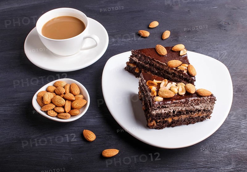 Chocolate cake with caramel, peanuts and almonds on a black wooden background. cup of coffee, close up