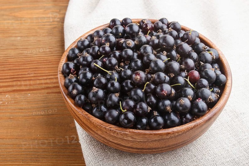 Fresh black currant in wooden bowl on wooden background. side view, close up