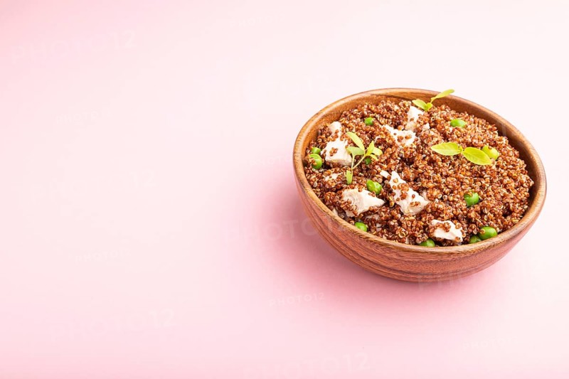 Quinoa porridge with green pea and chicken in wooden bowl on a pastel pink background. Side view, close up, copy space