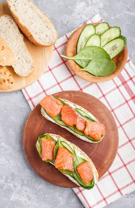 Smoked salmon sandwiches with cucumber and spinach on wooden board on a gray concrete background. top view, flat lay