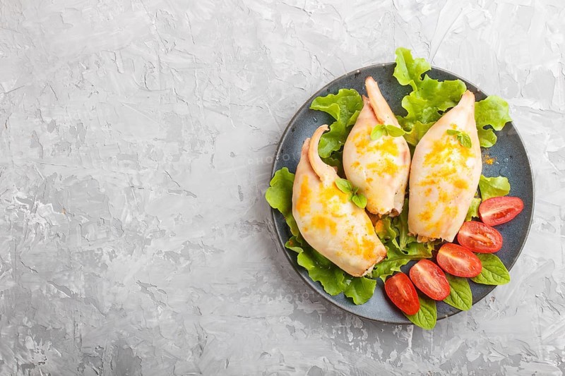Stuffed baked squid with greens on a blue ceramic plate on a gray concrete background, top view, flat lay, copy space