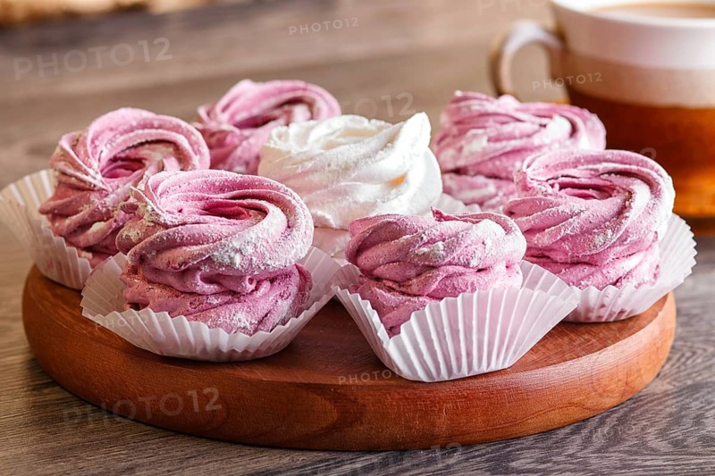 Pink and white marshmallows (zephyr) on a round wooden board with cup of coffee on a gray wooden background