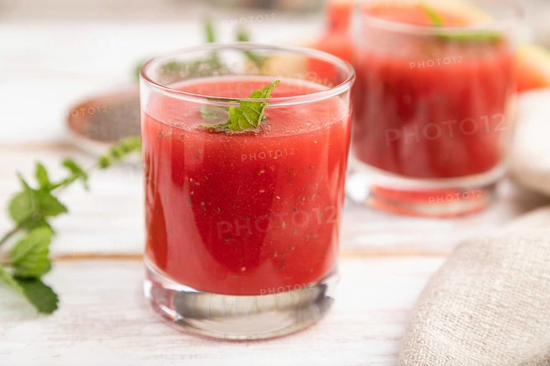 Watermelon juice with chia seeds and mint in glass on a white wooden background with linen textile. Healthy drink concept. Side view, close up, selective focus