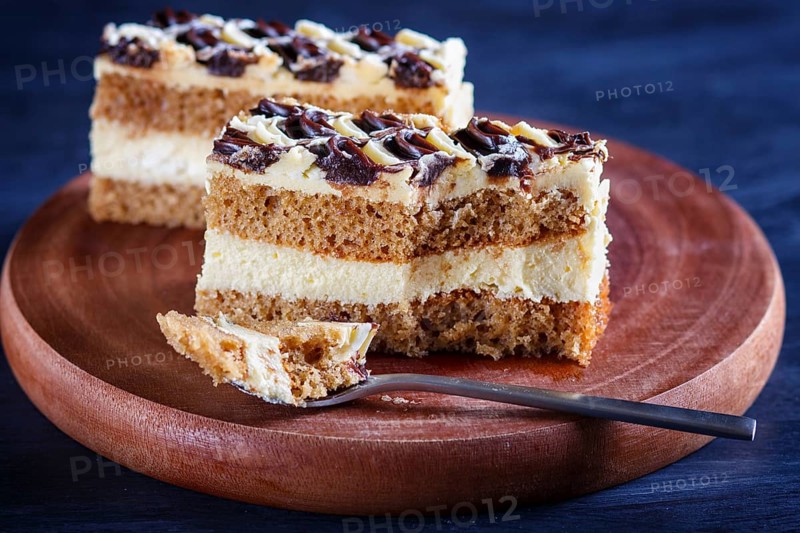 A piece of cake with milk and butter cream cutted with spoon on a wooden kitchen board, close up, selective focus, black background
