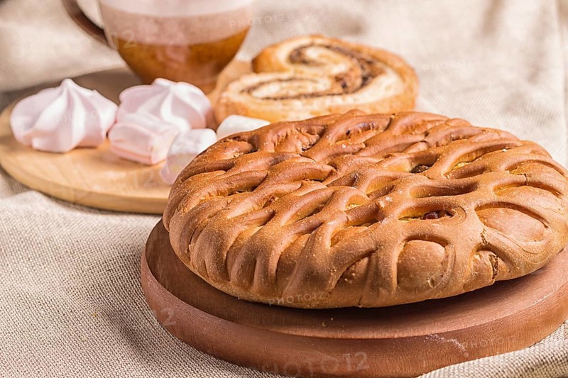 Sweet buns, meringues and coffee cup on a wooden board and linen tablecloth