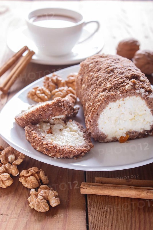 Roll cake with curd and walnuts isolated on white wooden background. close up