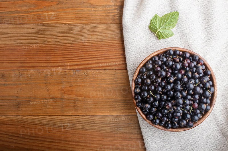 Fresh black currant in wooden bowl on wooden background. top view, flat lay, copy space