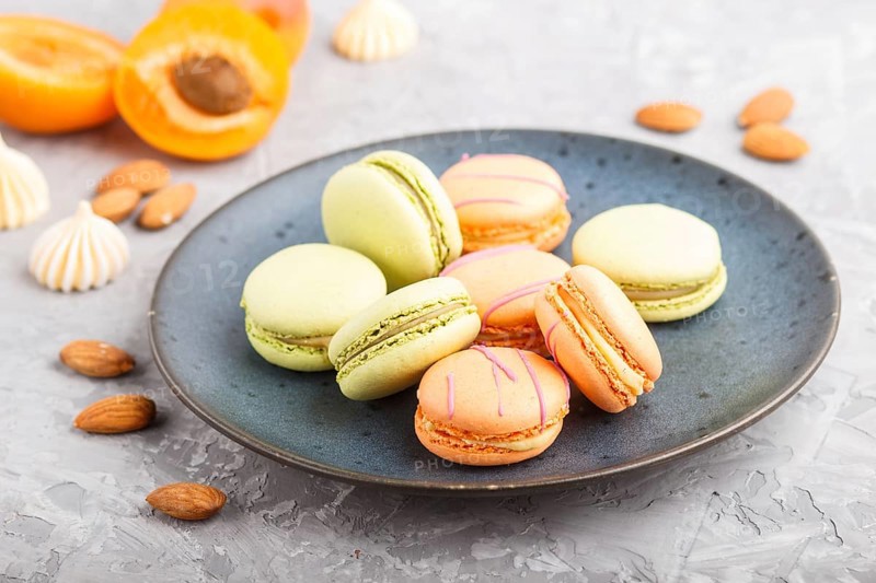 Orange and green macarons or macaroons cakes on blue ceramic plate on a gray concrete background. side view, close up, selective focus