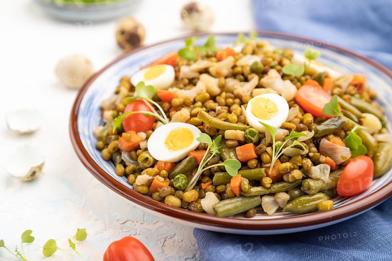 Mung bean porridge with quail eggs, tomatoes and microgreen sprouts on a white concrete background and blue textile. Side view, close up, selective focus