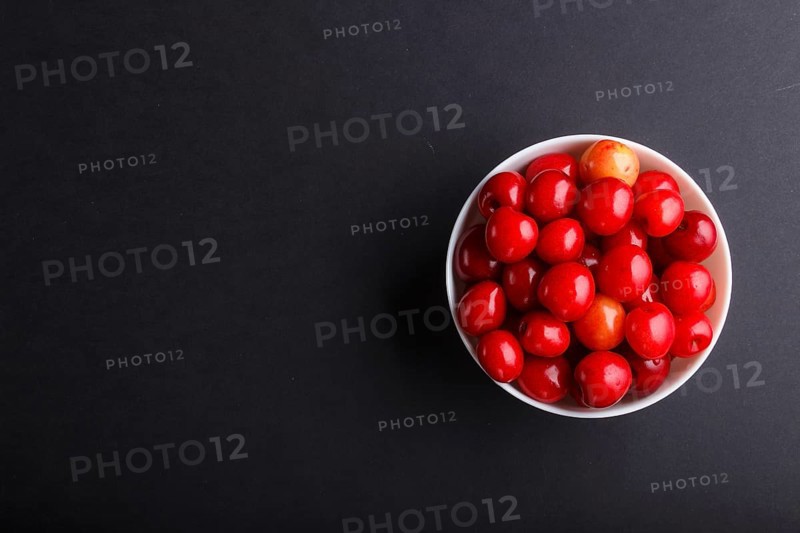 Fresh red sweet cherry in white bowl on black background. top view, flat lay, copy space