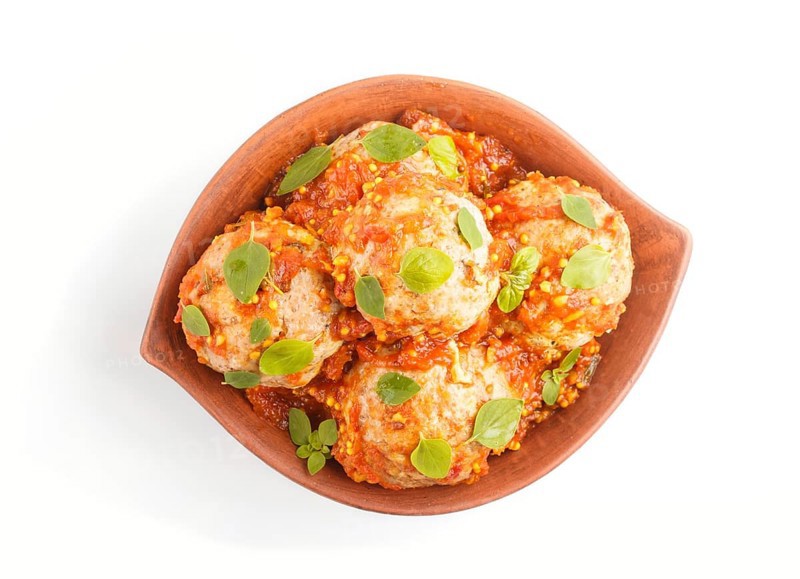 Pork meatballs with tomato sauce, oregano leaves, spices and herbs in clay bowl isolated on white background. top view, close up