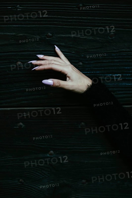 A hand with lavender nails against a dark wooden background evoking a mysterious elegance
