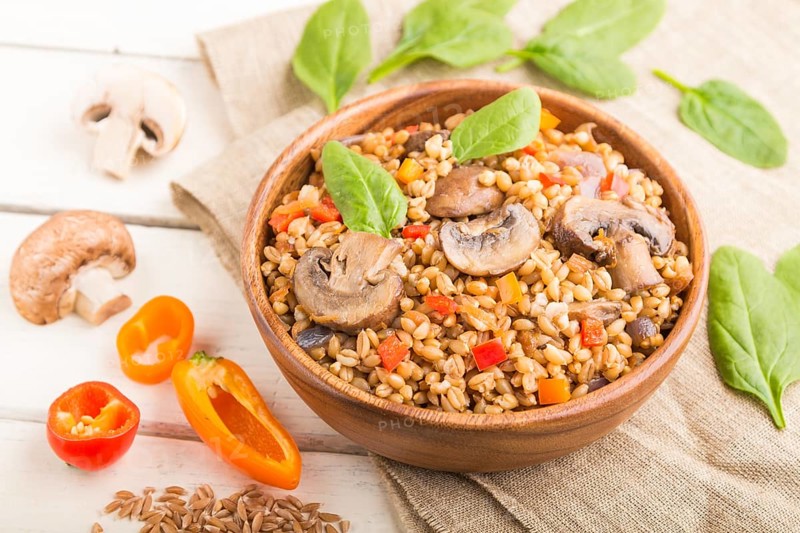 Spelt (dinkel wheat) porridge with vegetables and mushrooms in wooden bowl on a white wooden background and linen textile. Side view, selective focus. Russian traditional cuisine