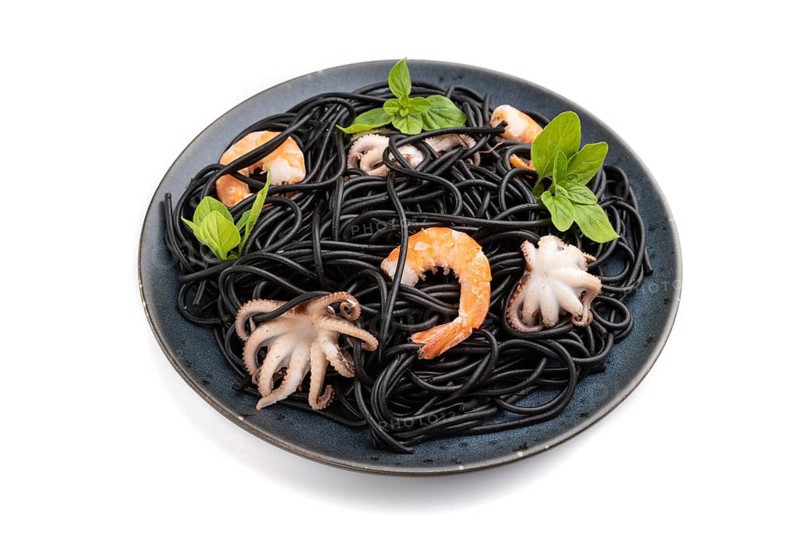 Black cuttlefish ink pasta with shrimps or prawns and small octopuses isolated on white background. Side view, close up