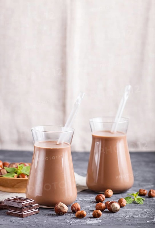 Organic non dairy hazelnut chocolate milk in glass and wooden plate with hazelnuts on a black concrete background. Vegan healthy food concept, close up, side view, copy space