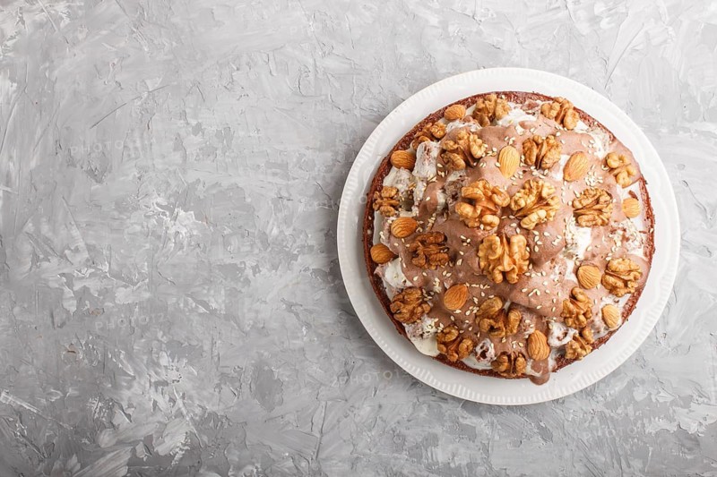 Homemade cake with milk cream, cocoa, almond, hazelnut on a gray concrete background with orange textile. Top view, flat lay, copy space