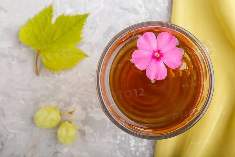 Glass of green grape juice with green textile and pink flower on a gray concrete background. Morninig, spring, healthy drink concept. Top view, close up, flat lay