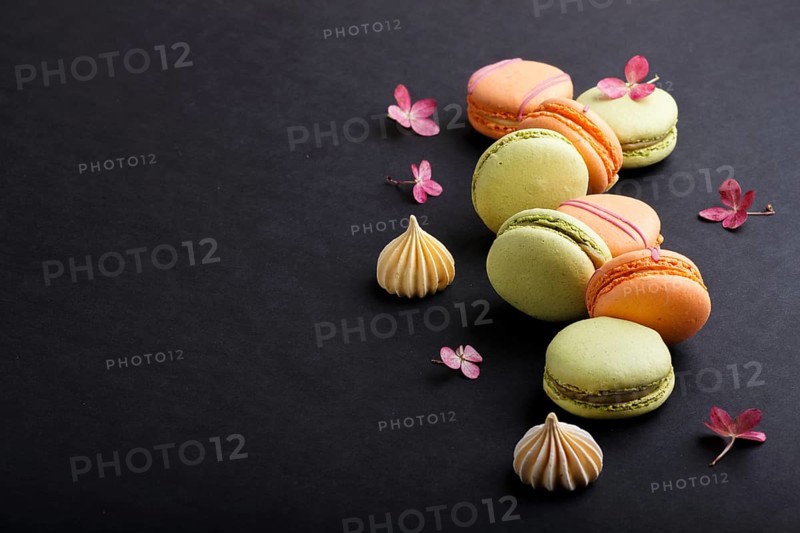 Orange and green macarons or macaroons cakes on black background. side view, close up, copy space