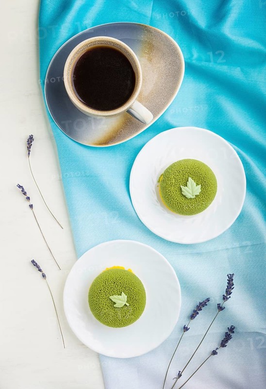 Green mousse cake with pistachio cream and a cup of coffee on a white wooden background and blue textile. top view, flat lay, close up