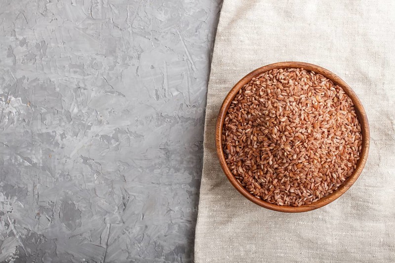 Wooden bowl with unpolished brown rice on a gray concrete background and linen textile. Top view, flat lay, copy space