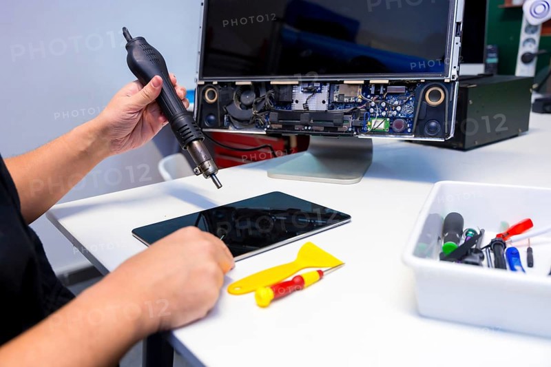 Side view of an unrecognizable technician fixing a computer component using a soldering iron in a workshop