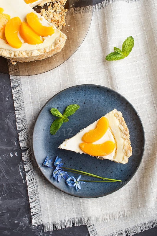 A piece of peach cheesecake on a blue ceramic plate with blue flowers on a linen napkin on a black concrete background. top view, copy space