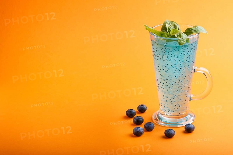 Glass of blueberry blue colored drink with basil seeds on orange background. Morninig, spring, healthy drink concept. Side view, selective focus, copy space