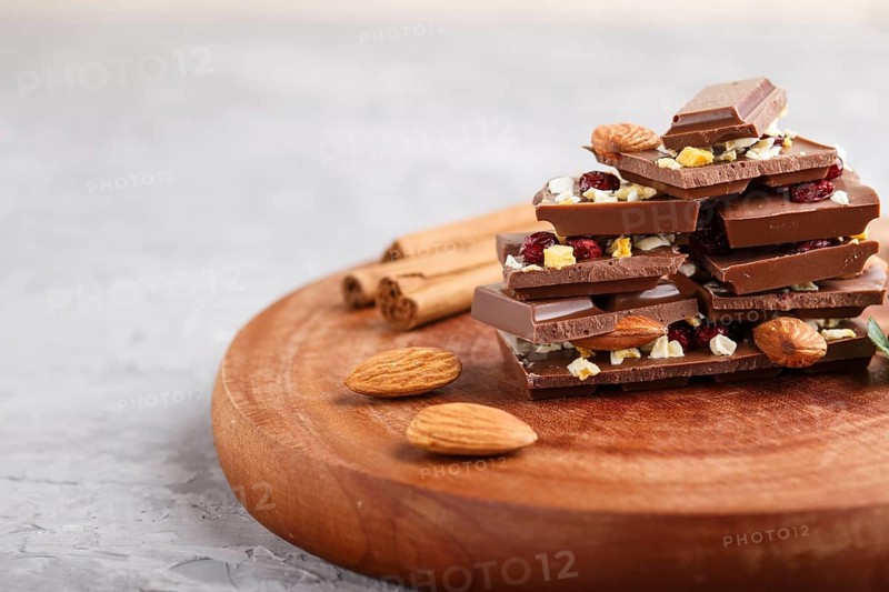 A pieces of milk chocolate with almonds and dried fruits on a brown wooden board on a gray concrete background. side view, close up, selective focus, copy space