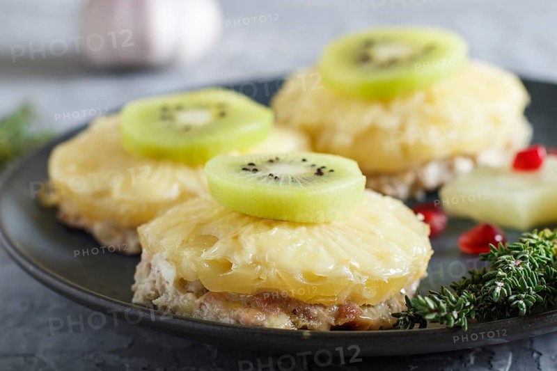Pieces of baked pork with pineapple, cheese and kiwi on gray background, side view, close up, selective focus