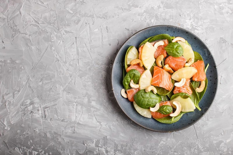 Fresh salmon with pineapple, spinach and cashew on a gray concrete background. Top view, copy space, flat lay